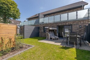 Una casa moderna con un balcone in vetro, un patio con mobili da esterno e un prato curato.