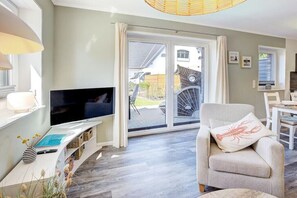A modern living room with a flat-screen TV, a comfortable armchair, and a sliding glass door leading to a patio. - Ording Seagull Island (St. Peter-Ording)