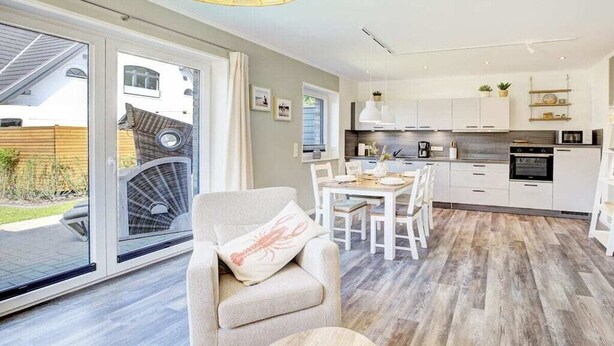 Een moderne keuken met witte kasten, een eethoek met een tafel en stoelen, en een grote schuifpui die leidt naar een buitenruimte.
