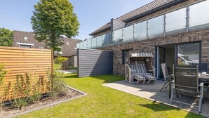 Een achtertuin met terras, houten omheining en een zithoek met stoelen en een tafel.