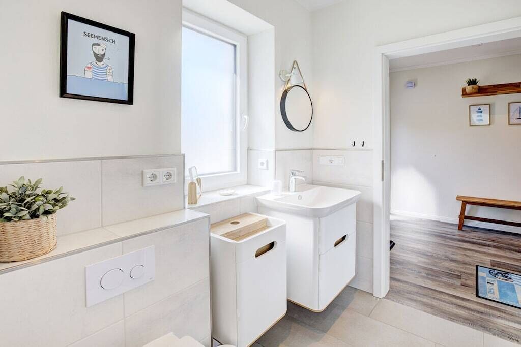 A modern bathroom with a large window, a wall-mounted mirror, and a framed picture.