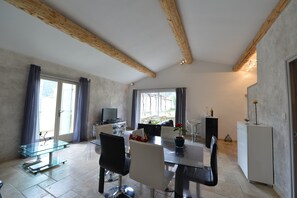 A modern dining area with a glass table, chairs, a television, and a view of the outdoors. - Just a short walk from the Luberon Mountains—accommodations for up to six people (Maubec)