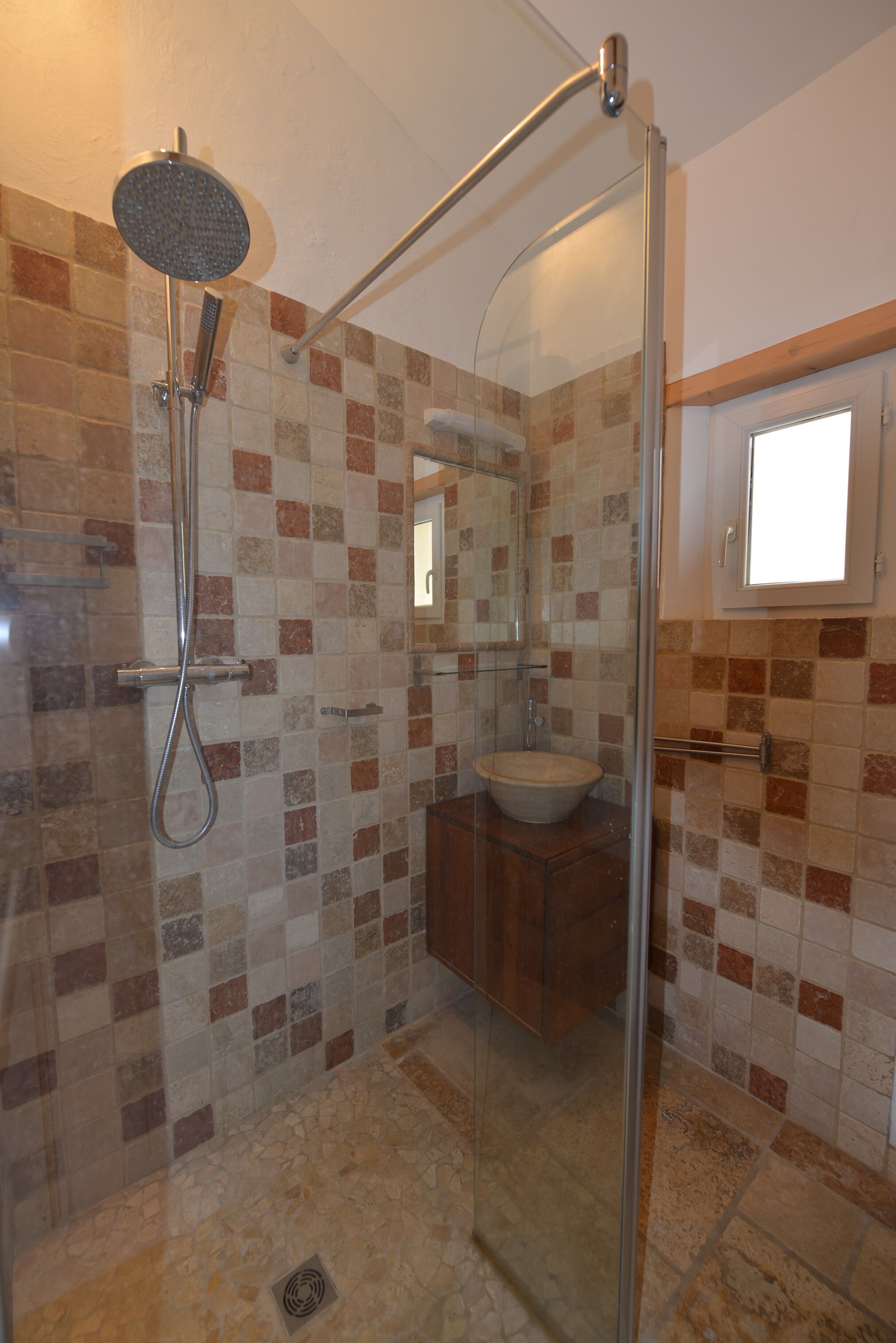 A bathroom with a glass-enclosed shower, a sink, and a mirror.