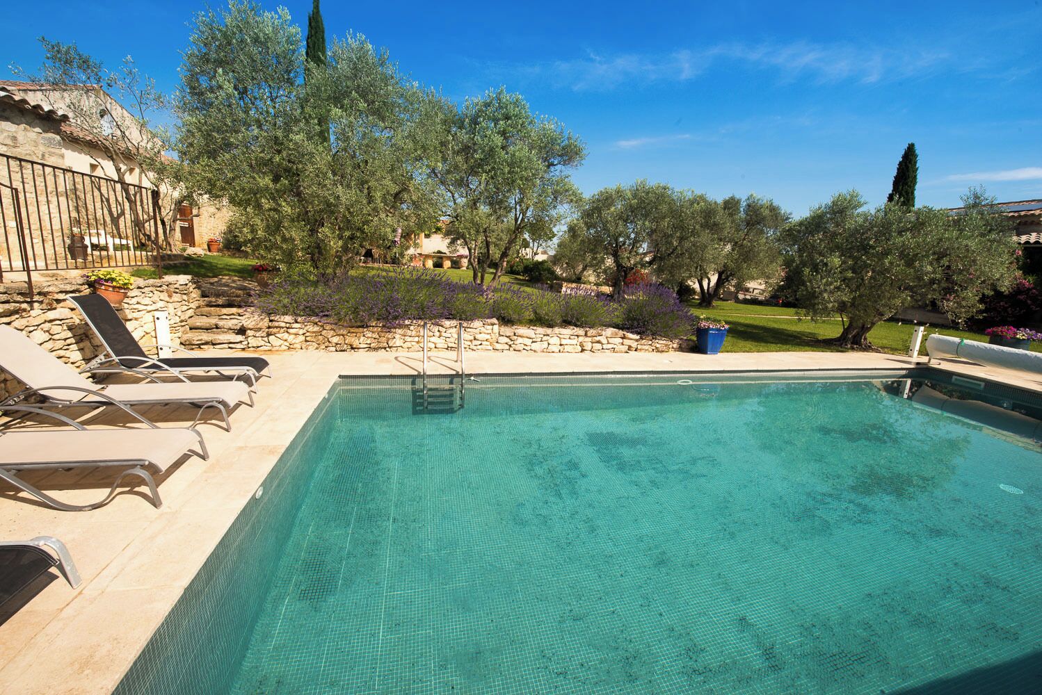 Una piscina con un solárium de piedra, rodeada de sillas de descanso y plantas en macetas.