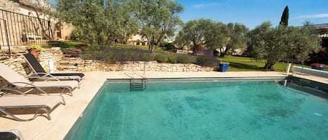 Una piscina con un solárium de piedra, rodeada de sillas de descanso y plantas en macetas.