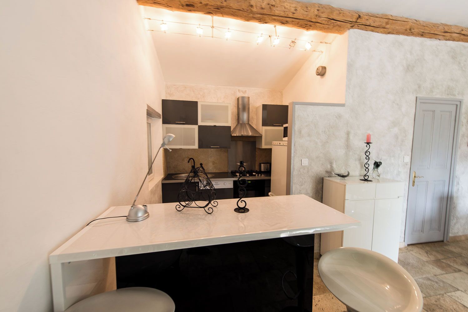 A compact kitchen with a central island, a stove, and a sink. There is a small dining area with a chair and a table.