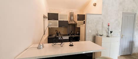 Cocina compacta con una isla central, estufa y lavamanos. Cuenta con un pequeño comedor con una silla y una mesa.