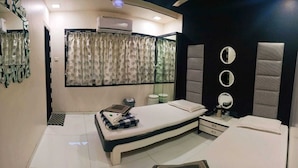 Quarto com cama, mesas de cabeceira, espelho e janela com cortinas.