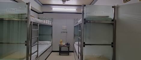 A narrow corridor with bunk beds on either side, a ceiling fan, and a small table with a kettle and cups.