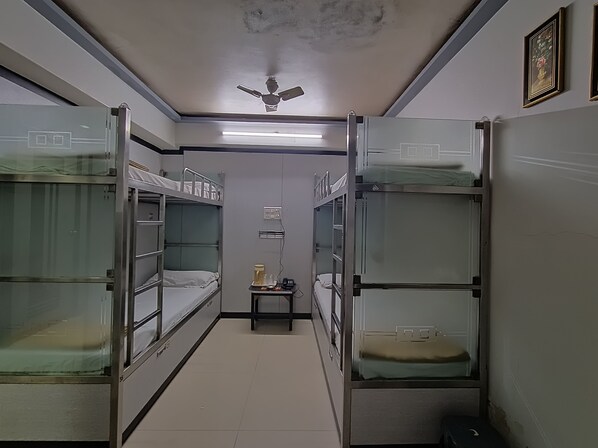 A narrow corridor with bunk beds on either side, a ceiling fan, and a small table with a kettle and cups.