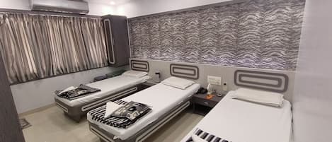 A hotel room with three single beds, a ceiling fan, an air conditioning unit, and a patterned wall.