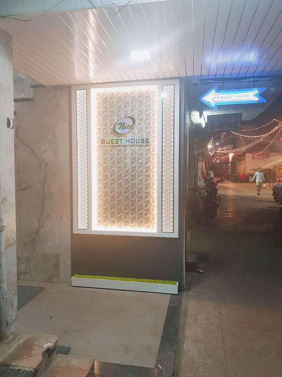 L’entrée d’une maison d’hôtes, avec un panneau indiquant la direction, un mur orné de motifs et un chemin pavé menant à l’extérieur.