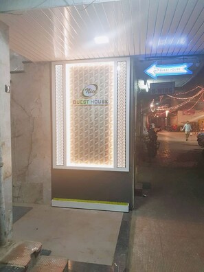 A guesthouse entrance with a sign indicating direction, a patterned wall, and a paved pathway leading outside. - Nice Guest House (Mumbai)