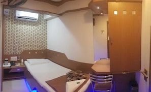A compact room with a bed, a small table, a cabinet, and a wall-mounted air conditioner. - Nice Guest House (Mumbai)