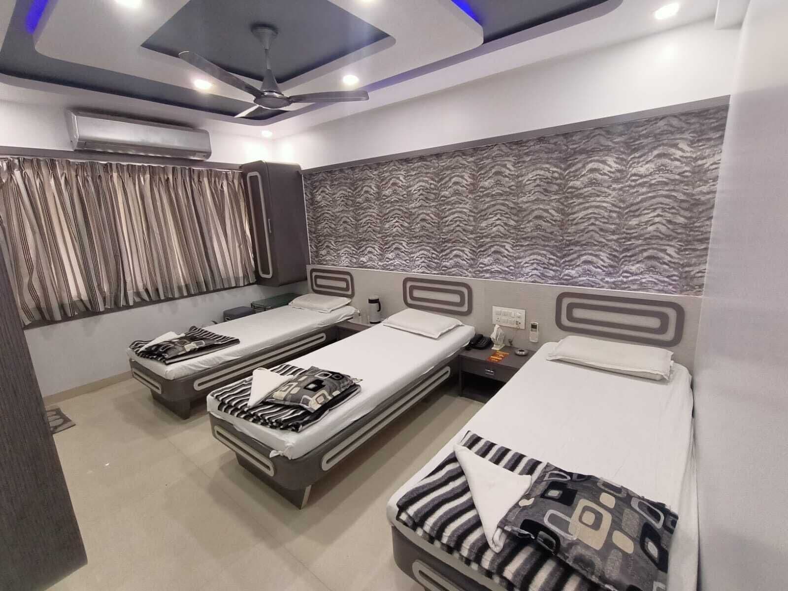 A hotel room with three single beds, a ceiling fan, and a patterned wall.