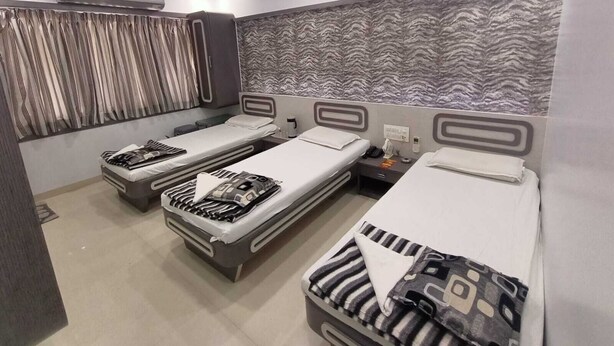 Quarto de hotel com três camas de solteiro, ventilador de teto e parede com padrão.