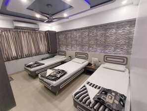 A hotel room with three single beds, a ceiling fan, and a patterned wall. - Nice Guest House (Mumbai)