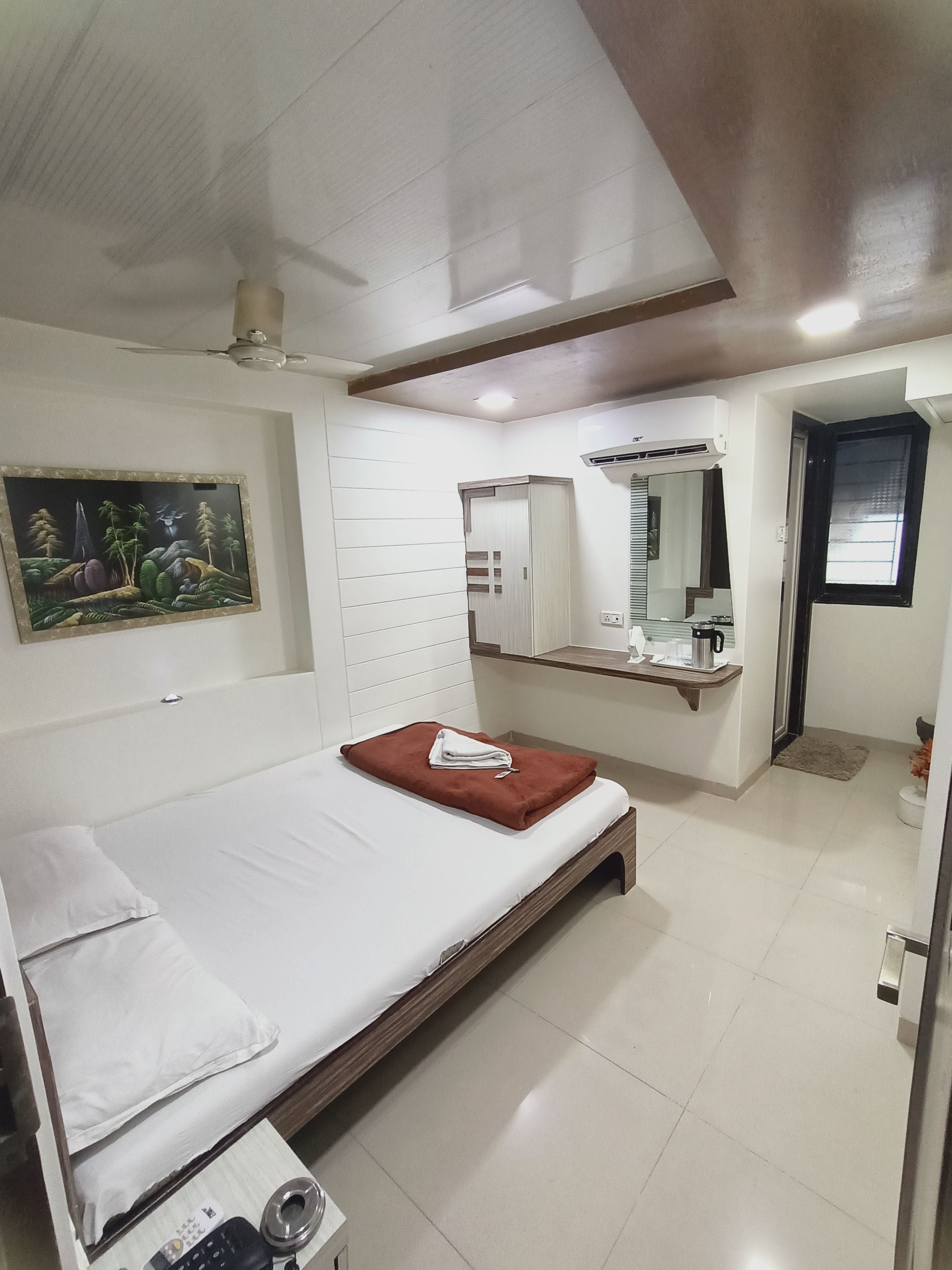 A hotel room with a bed, a bedside table, a mirror, and a window.