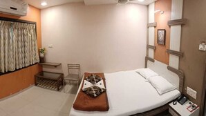Quarto de hotel com cama, mesa pequena, cadeira, mesa de cabeceira e cortina.