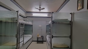 Um corredor estreito com beliches em ambos os lados, um ventilador de teto e uma pequena mesa com uma luminária.