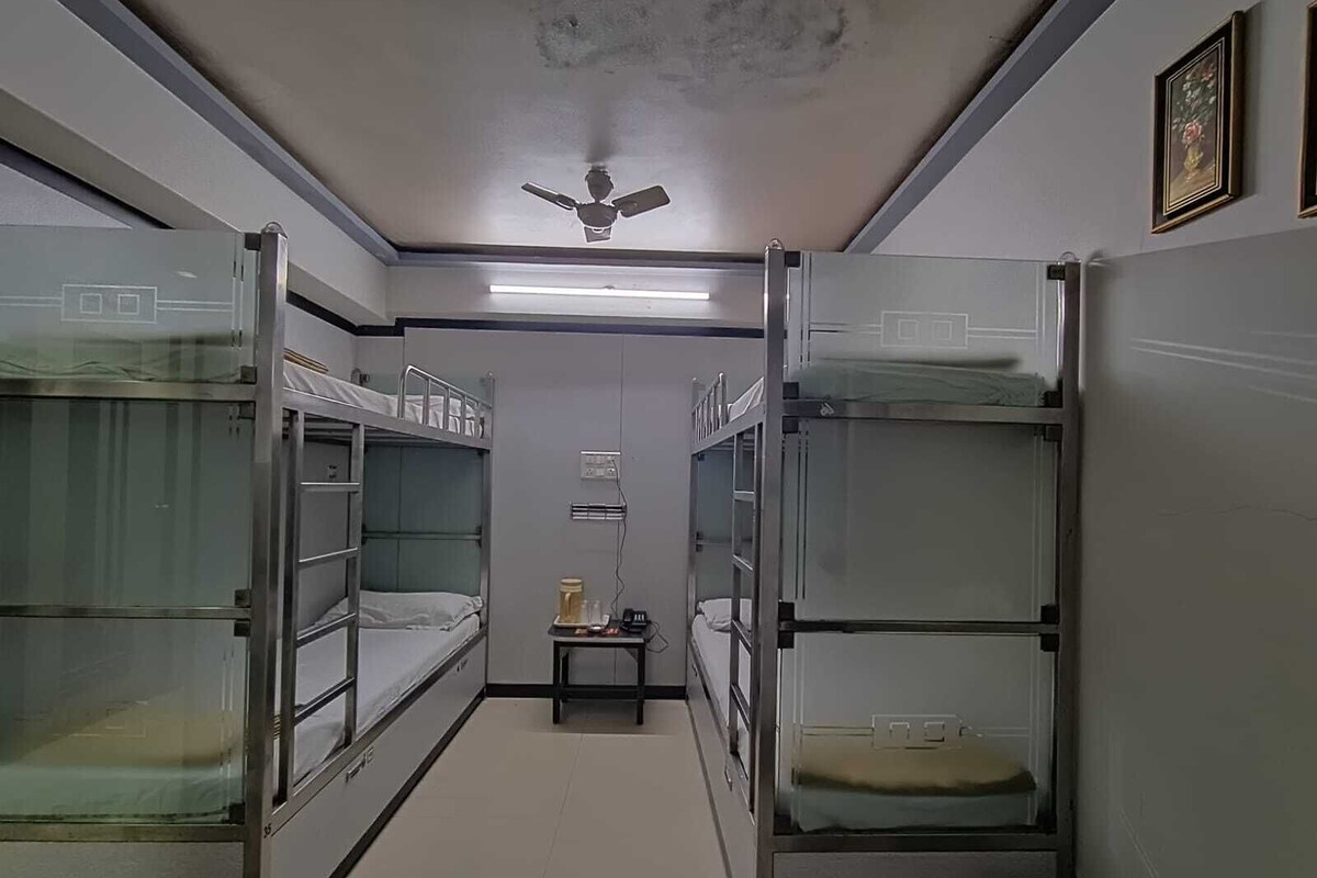 A narrow corridor with bunk beds on either side, a ceiling fan, and a small table with a lamp.