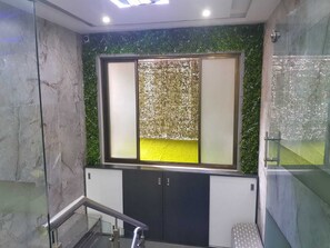 A modern bathroom with a glass shower enclosure, a marble wall, and a green decorative wall panel. - Nice Guest House (Mumbai)
