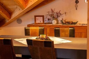 Ein Essbereich mit einem Tisch für vier Personen, Holzsesseln, einer Kerzenarrangements und einem Wandregal mit Dekoration.