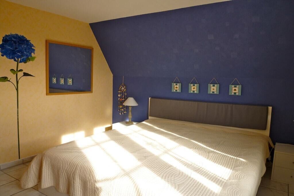 A bedroom with a bed, a nightstand, a lamp, a wall clock, and a framed picture.