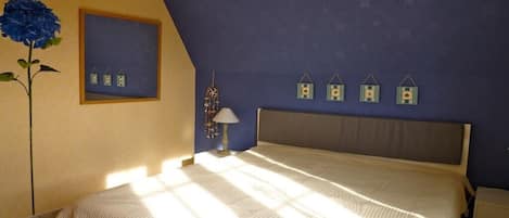 A bedroom with a bed, a nightstand, a lamp, a wall clock, and a framed picture.