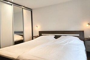 A hotel room with a bed, a nightstand, a wall-mounted light, and a sliding door closet. - DO01 Holiday bungalow near the beach and city (DOMBURG)