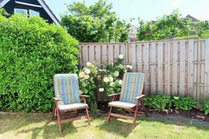 Two striped chairs in a garden with a wooden fence and lush greenery. - DO01 Holiday bungalow near the beach and city (DOMBURG)