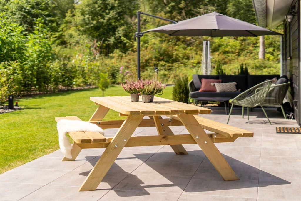 A wooden picnic table with benches, an umbrella, and a potted plant in a garden setting.
