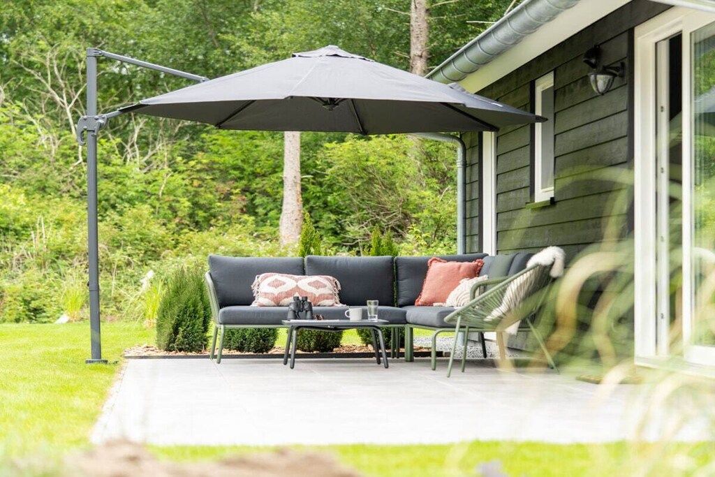 An outdoor seating area with a sofa, chairs, and a table, under a large umbrella, with a house in the background.