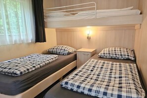 A room with two single beds, a bunk bed above, a bedside table, and a window with curtains. - Holiday home with 1 bedroom (Oostkapelle)