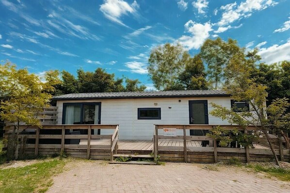A single-story mobile home with a fenced front yard, a paved driveway, and a clear sky. - Holiday home with 1 bedroom (Oostkapelle)