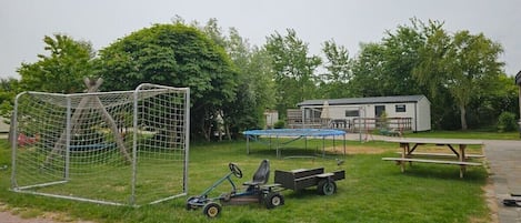 Un espacio cubierto de césped con un arco de fútbol, un remolque pequeño y una mesa de picnic.