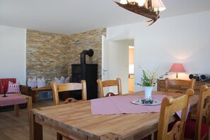 Un comedor con una mesa de madera, sillas, un muro de piedra y una estufa negra.