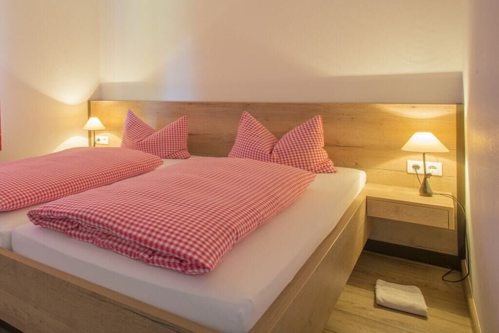 Een tweepersoonsbed met geruit beddegoed, nachtlampjes en een houten hoofdbord.