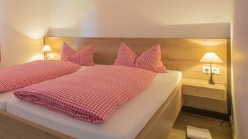 Een tweepersoonsbed met geruit beddegoed, nachtlampjes en een houten hoofdbord.