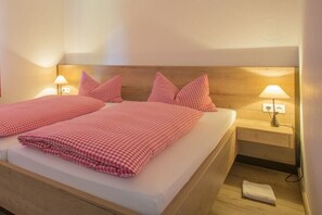 Cama doble con ropa de cama a cuadros, lámparas de noche y cabecera de madera.