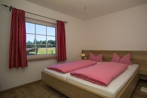 Ein Schlafzimmer mit großem Fenster, einem Bett mit karierter Bettwäsche und einem Holzkopfende.
