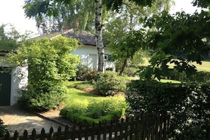 Ein weißes Gebäude mit einem Ziegeldach, umgeben von üppiger Vegetation und einem Holzzaun.
