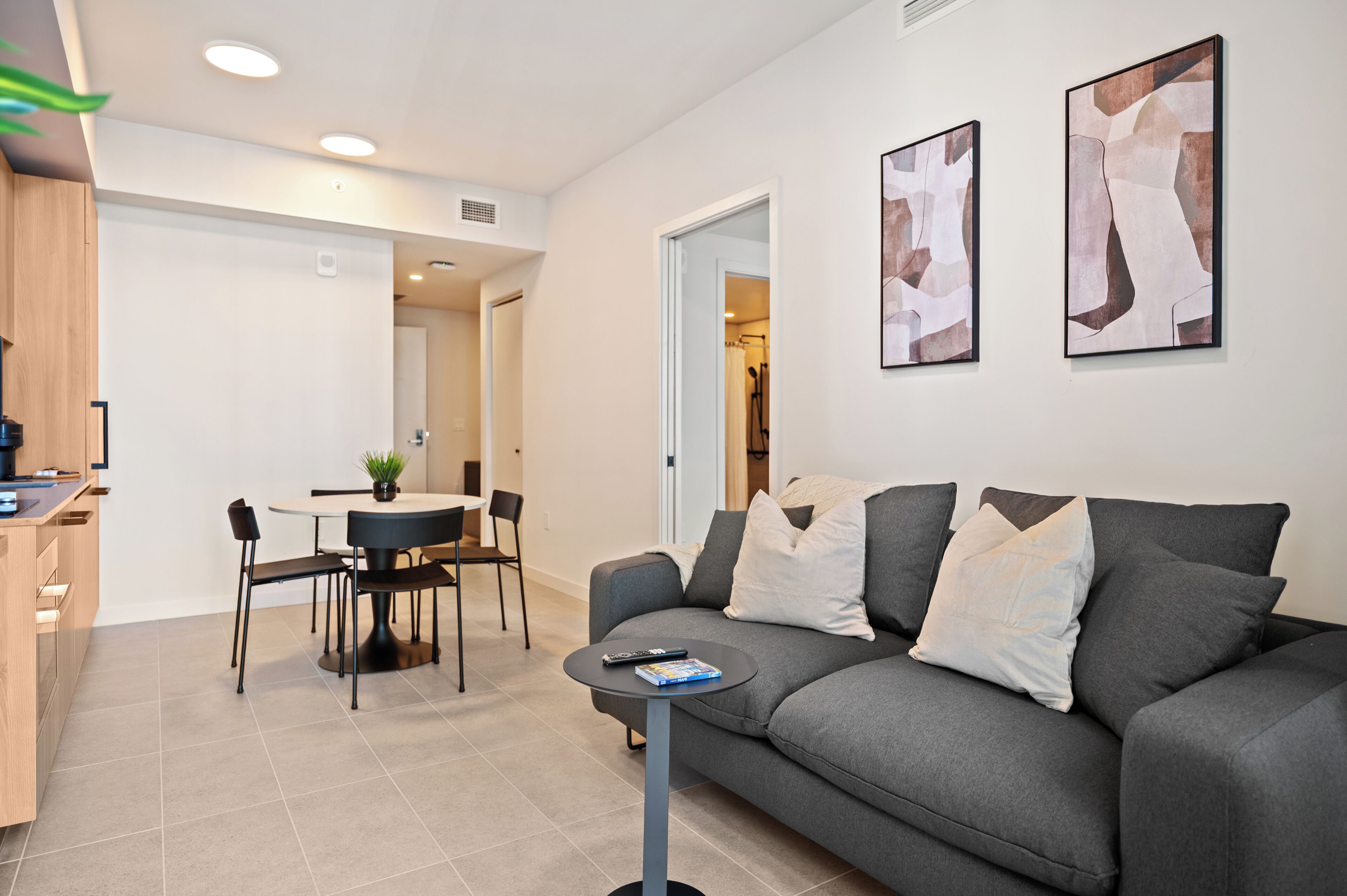 Una sala de estar moderna con un sofá gris, una mesa de comedor con sillas y dos cuadros abstractos en la pared.