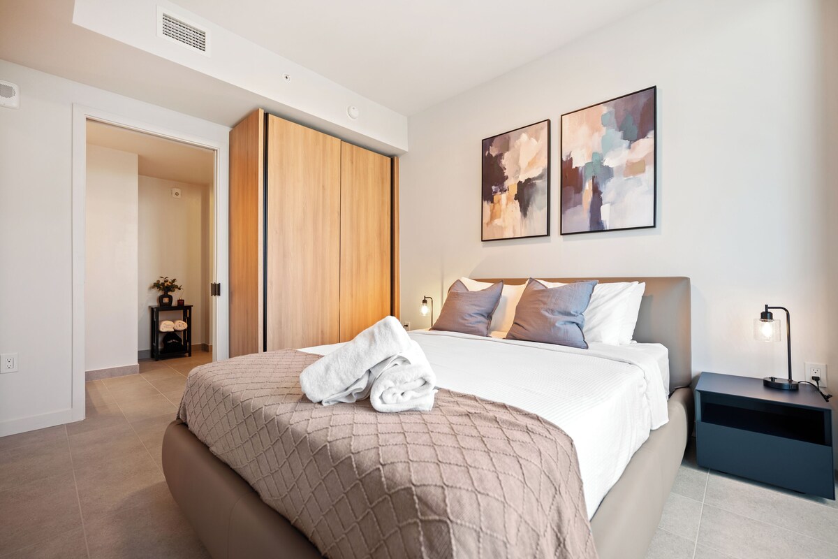 Una habitación de hotel moderna con una cama, una mesita de noche, una lámpara y arte abstracto en la pared.