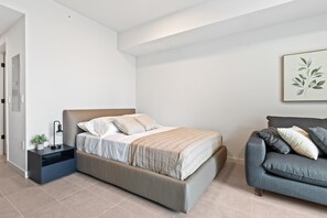 Un dormitorio moderno con una cama, una mesita de noche y un sofá gris.