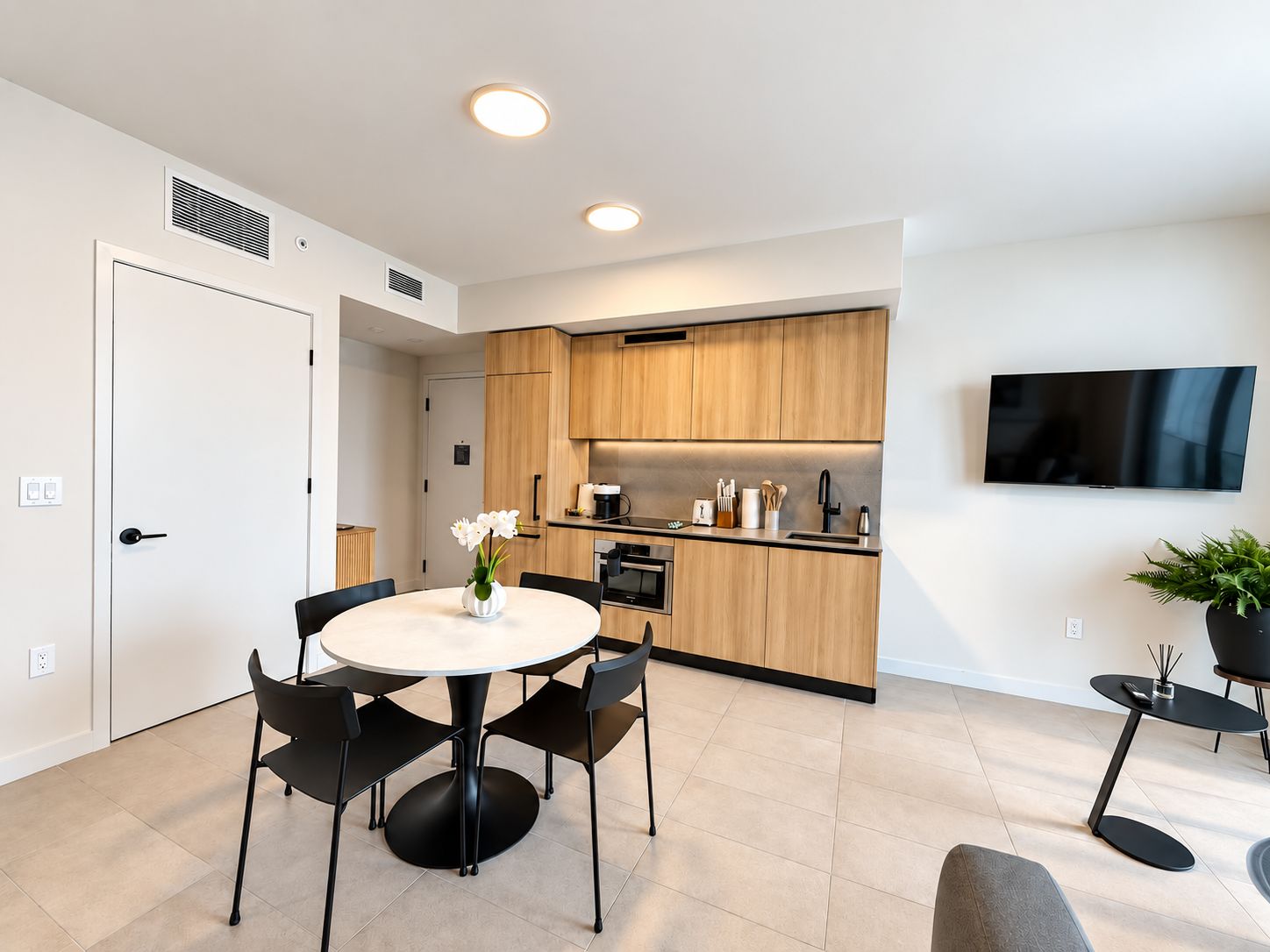 A modern kitchen with wooden cabinets, a built-in oven, and a flat-screen TV mounted on the wall.