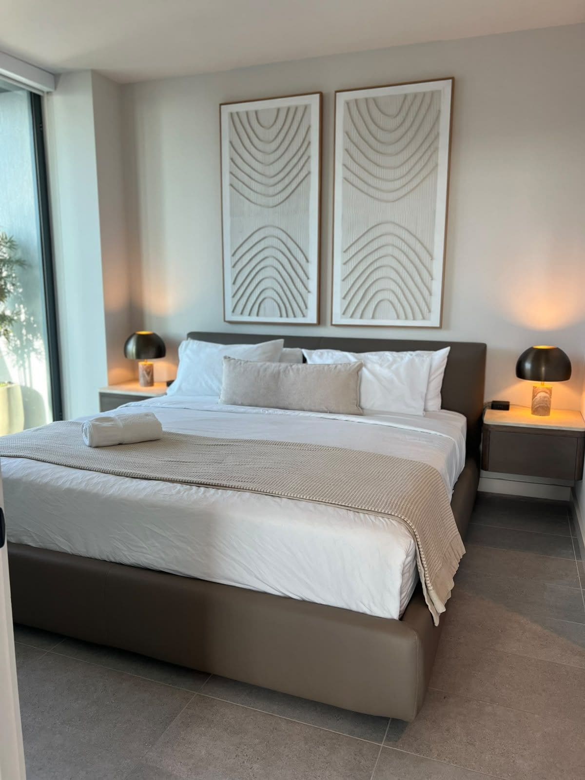 A modern bedroom with a large bed, two bedside tables with lamps, and abstract wall art.