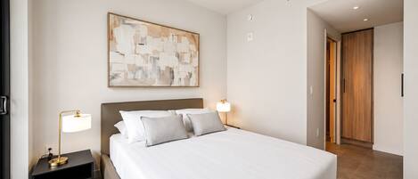 Una habitación de hotel moderna con una cama grande, lámparas de noche, un cuadro en la pared y una puerta de madera.