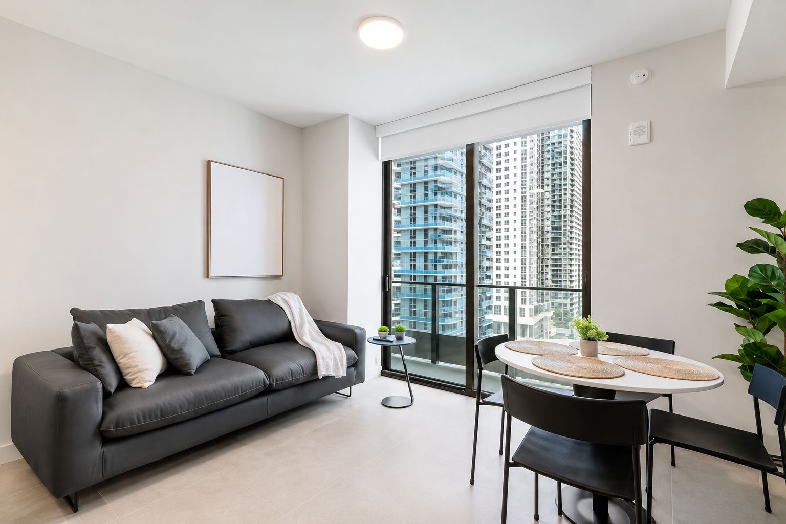 Uma sala de estar moderna com um sofá cinzento, uma mesa de jantar com cadeiras e uma grande janela com vista para a cidade.