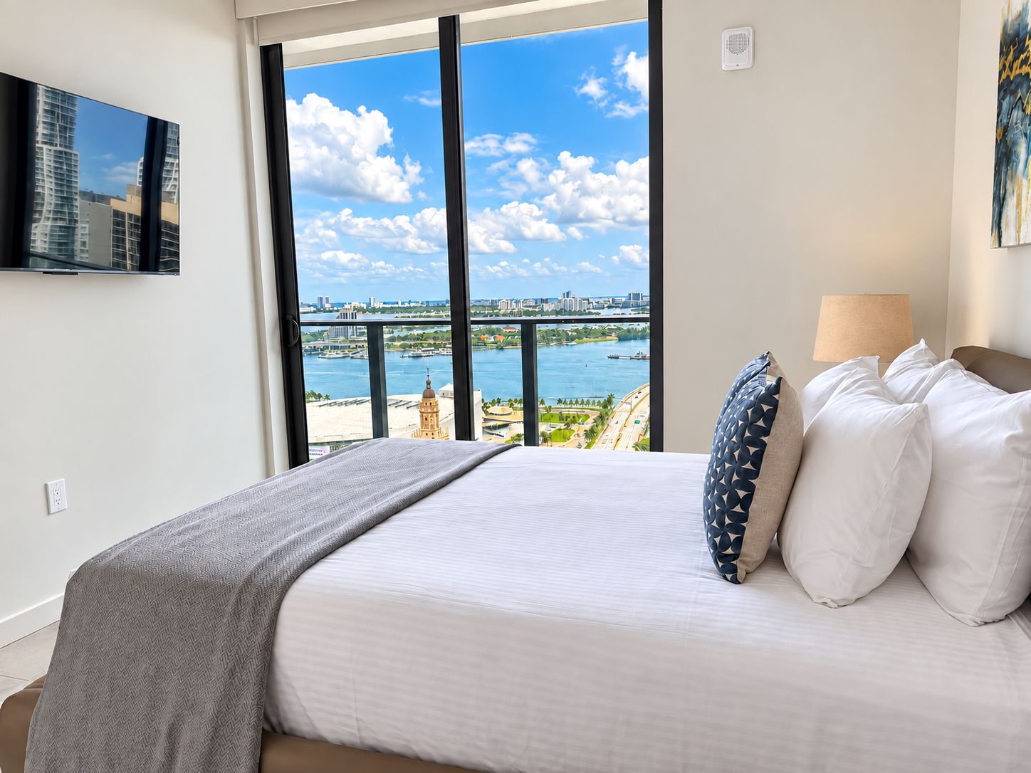 A hotel room with a large window offering a view of a city skyline and water.